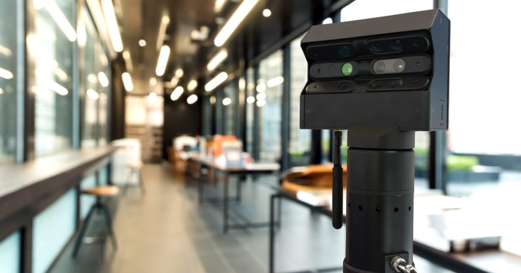 A 3D scanner set up in a long hallway. The background is blurred, but you can see a few tables behind the scanner.