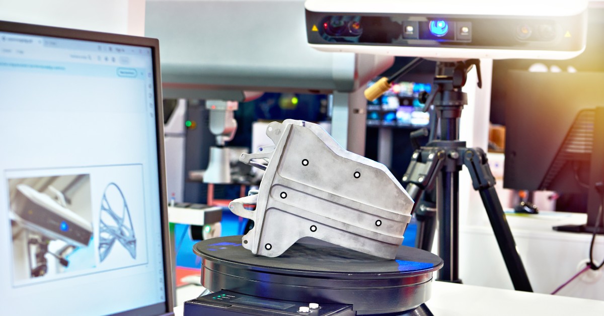 A metal component sitting on a pedestal while getting scanned by a laser scanner. There is a computer screen nearby.