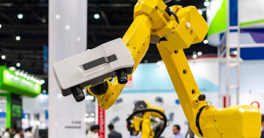 A 3D laser scanner attached to a large yellow arm. The scanner is currently facing downward at something below it.