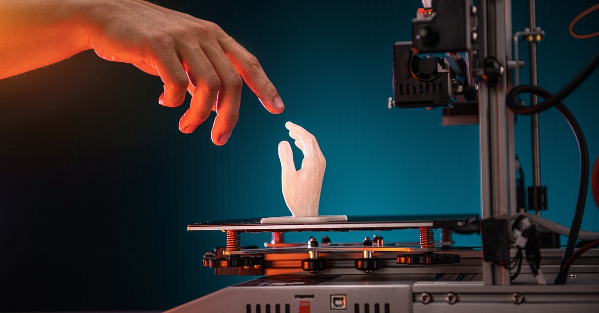 Someone stretching out their hand to touch a 3D printed hand. The printed hand is still sitting on the printer.